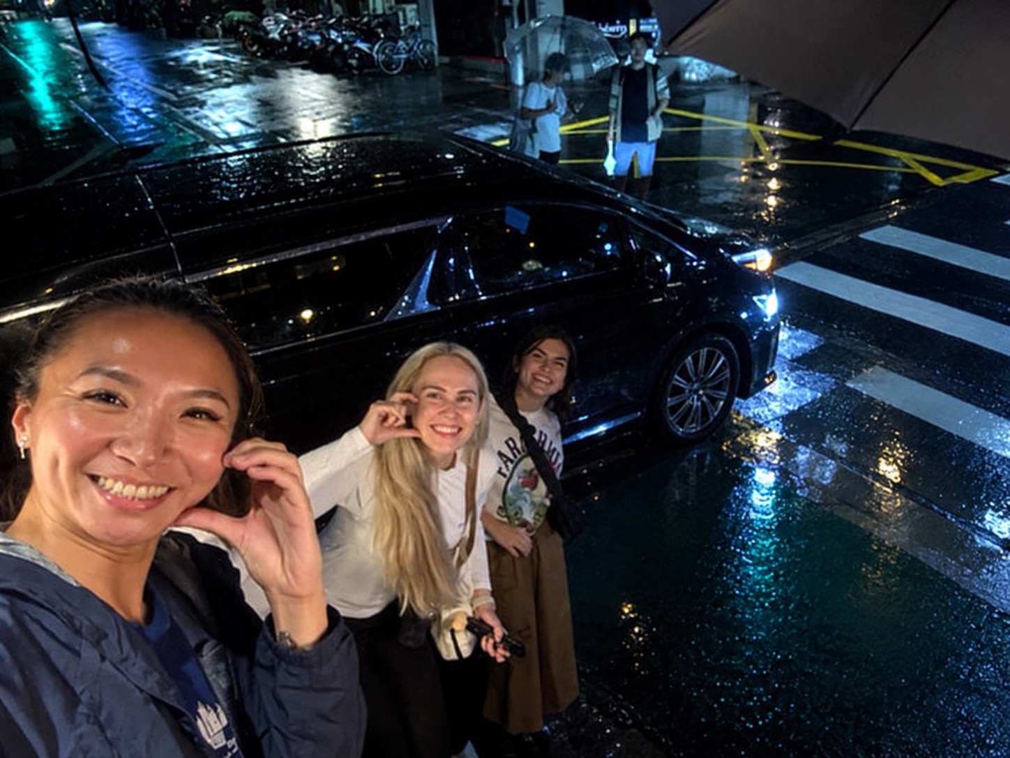 Three women smiling on a rainy night out