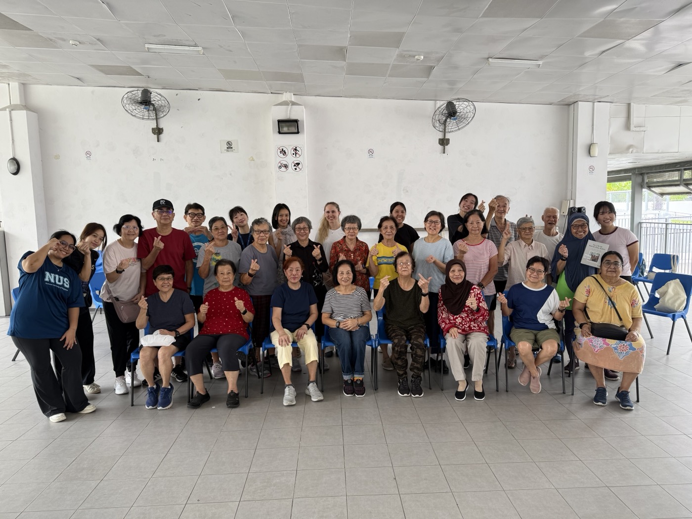 A community exercise class with older adults, all making finger hearts