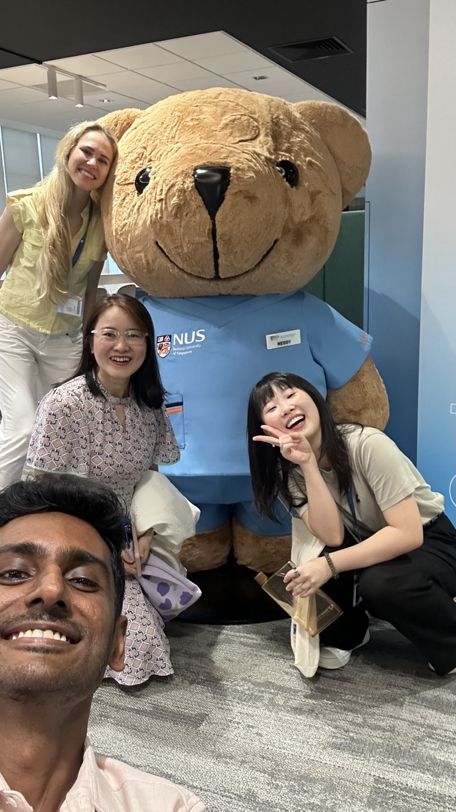 Friends posing with a giant teddy bear in NUS scrubs